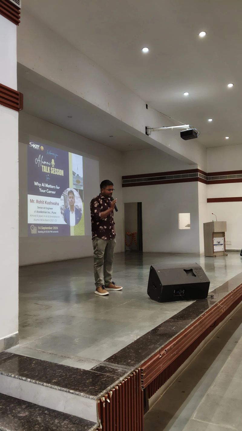 Rohit speaking on stage at the Alumni Talk Session, with the session poster projected behind him